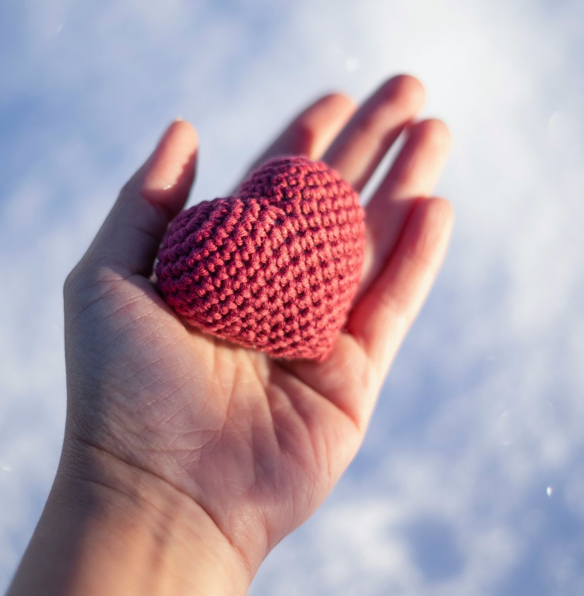 Main ouverte tenant un petit cœur rouge en crochet, symbole d’émotion, d’amour et de fait main.