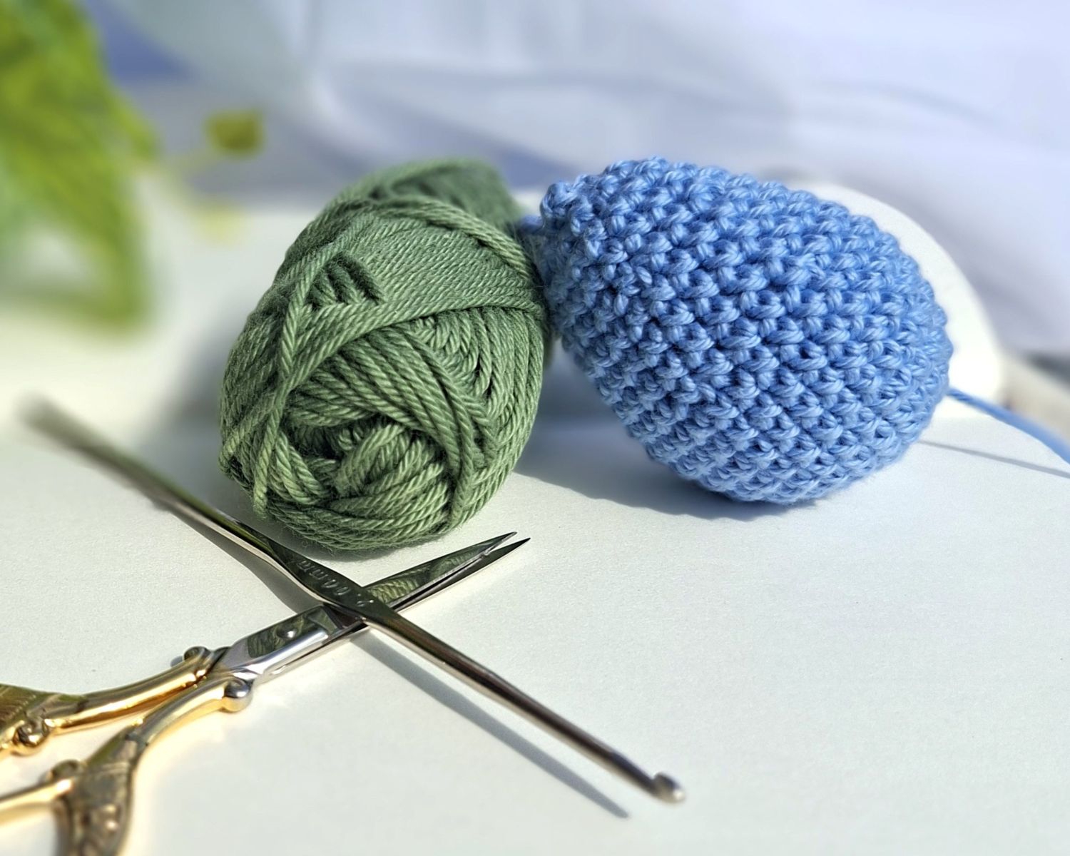 Goutte bleue crochetée à côté d’un fil vert et d’un crochet doré.