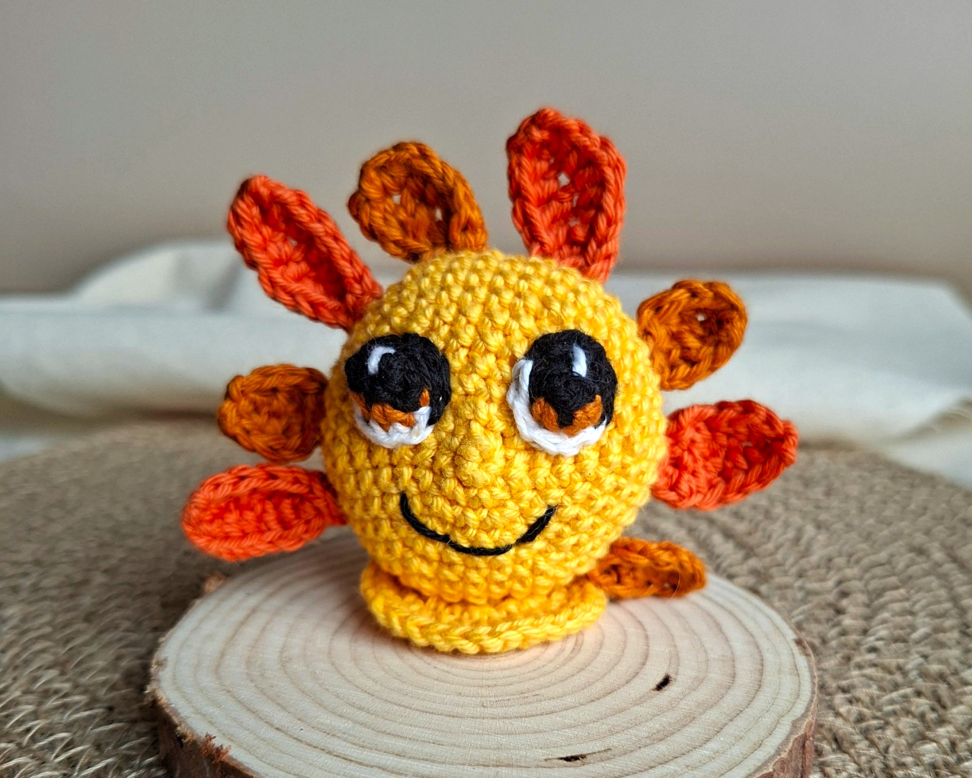 Amigurumi Soléa représentant un petit soleil, incarnant la joie, crocheté à la main dans les tons jaune et orange