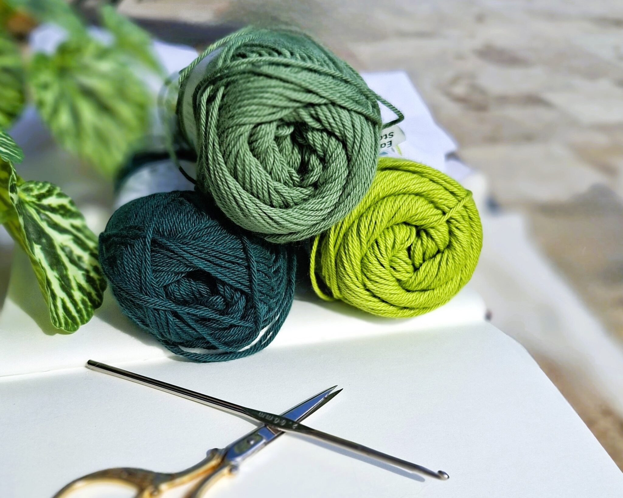 Trois pelotes de laine vertes posées sur un carnet, avec un crochet et des ciseaux, illustrant l’influence des couleurs sur les émotions