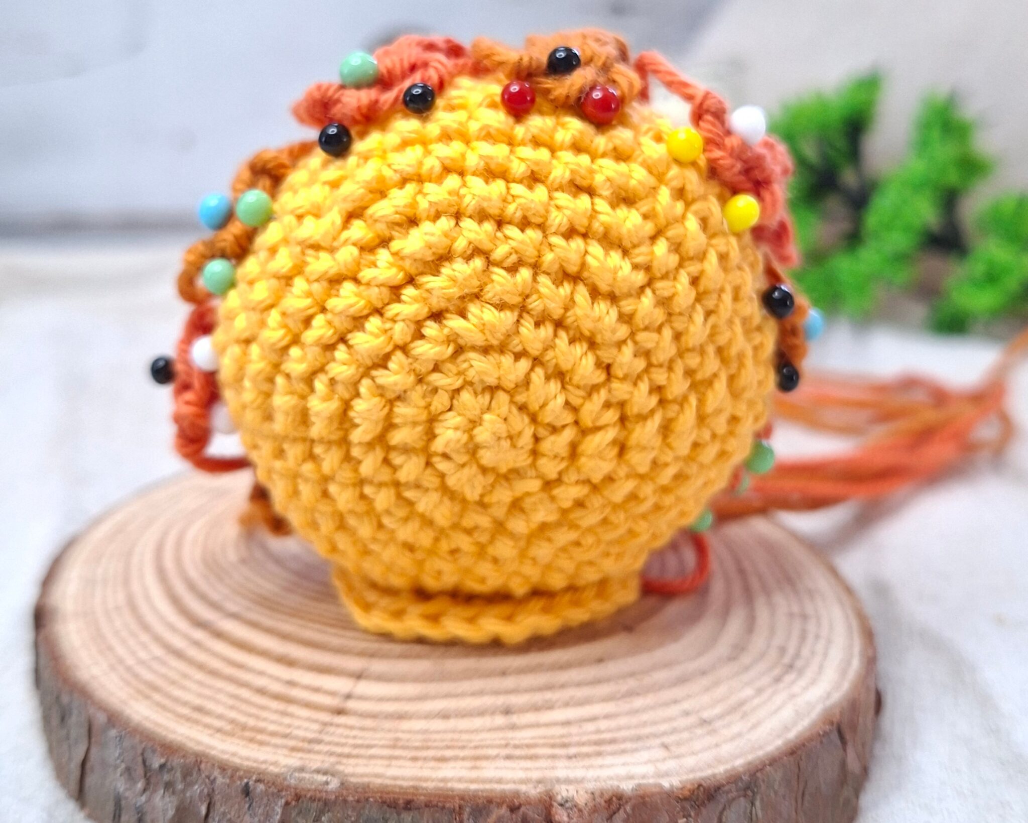 Amigurumi jaune en cours d’assemblage avec rayons orange fixés par des épingles, posé sur un socle en bois clair, création artisanale au crochet.