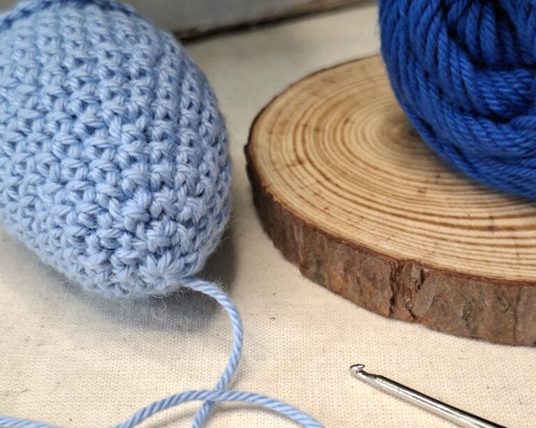 Ouvrage en crochet bleu clair avec fil, crochet métallique et pelote bleu profond sur socle bois, illustrant la symbolique du bleu et de la tristesse.