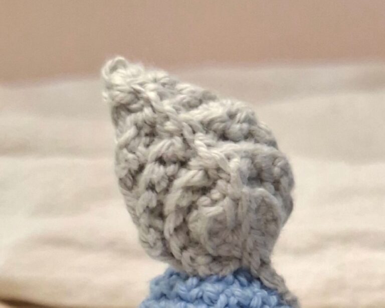 Accessoire au crochet en forme de plume grise, symbole de douceur et de légèreté dans l’univers de Plumélia.