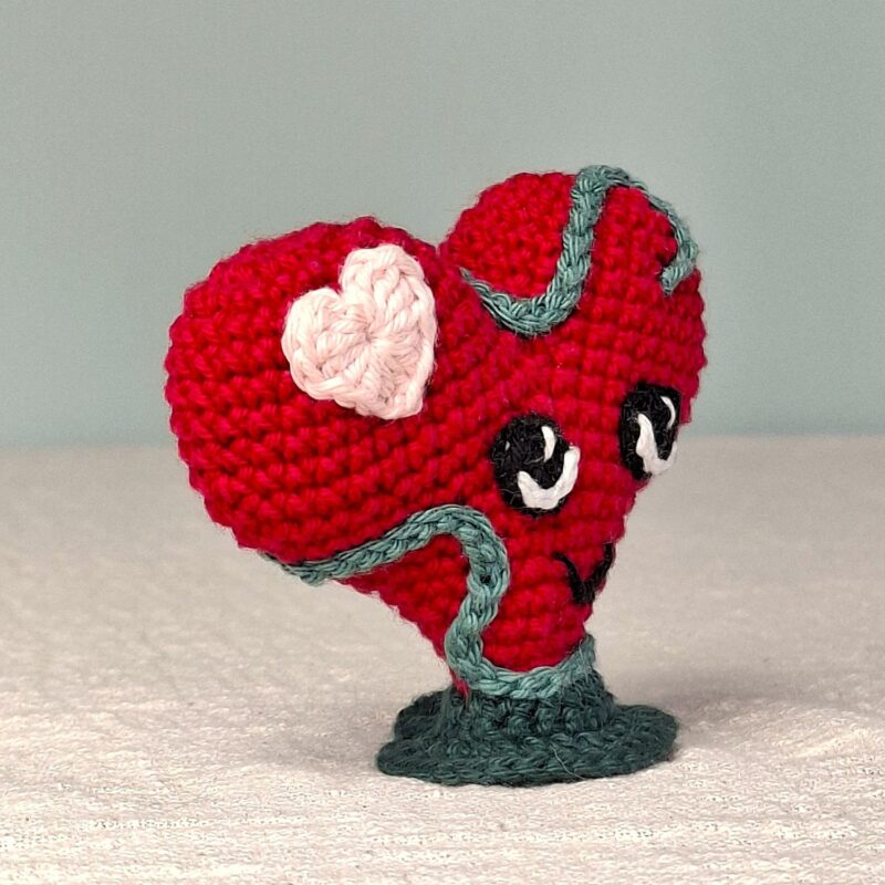 Amigurumi Lianis cœur rouge avec cœur blanc et liane verte, sur socle vert, vue de trois quarts