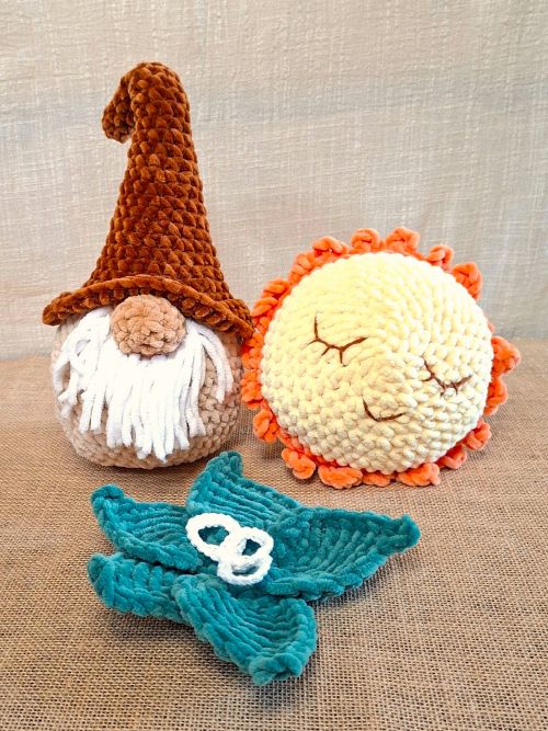 Trois Veilleurs d’Hiver crochetés : Naélis le gnome, Lumino la lumière ronde et Sélia la feuille turquoise en chenille, posés sur une toile de jute.